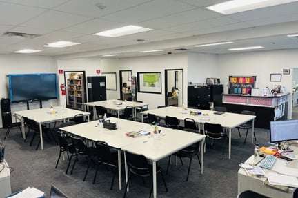 Wide view of a Taylion classroom with student tables, chairs, learning supplies, whiteboards, and organized work areas in a bright indoor space