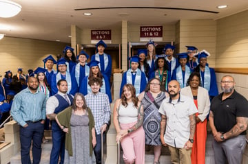 staff and students in graduation cap and gowns standing on stairs outside of a building