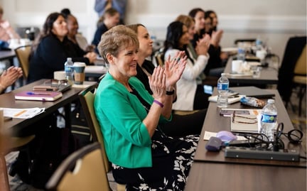Leadership at a conference, sitting at a table and clapping to a presentation being given