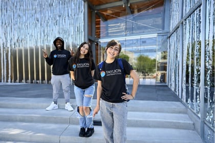 Three teen students wearing black Taylion Academy shirts standing on stairs outside of a building
